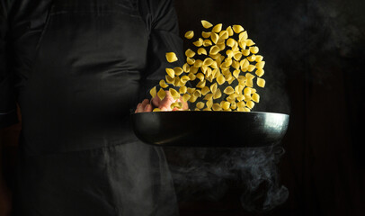 The chef is preparing pasta in a frying pan. Low key concept of cooking pasta in the kitchen with...