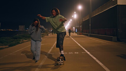 Teen skaters riding skate boards enjoying night street. Man balancing skateboard
