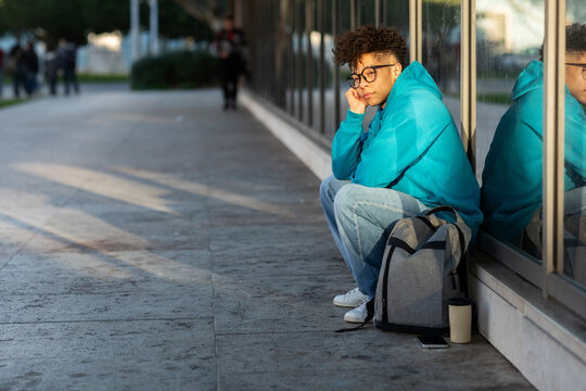 Unhappy black student guy sitting with backpack outdoors at night