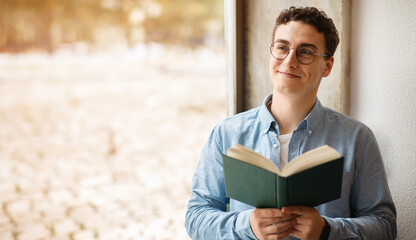 A contented young man with curly hair and round glasses is engrossed in reading a book