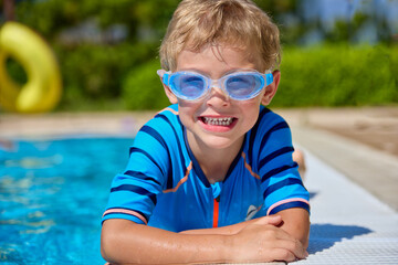 Close-up of a cute happy child lying on a hot sunny day by the cool water of the outdoor pool....