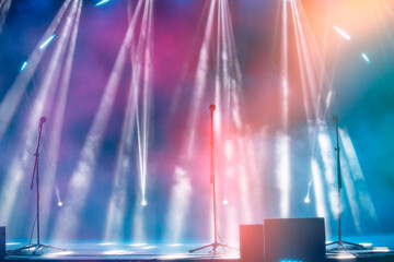 Blurred rays of light from stage spotlights on a multi-colored stage background with microphones....