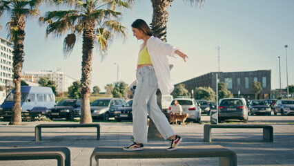 Sportive girl holding skateboard crossing benches. Woman waiting friend walking