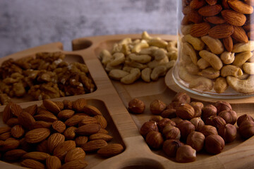  Close-up of walnuts, cashews, almonds and hazelnuts on a wooden tray. On a wooden plate there is a transparent glass jar filled with assorted nuts.