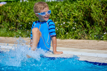 Cute boy plays in the water in the outdoor pool during the summer holidays. Against the background...
