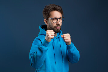 Determined man wearing eyeglasses and hoodie raising his fists in defensive pose