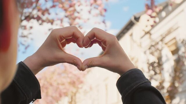 I Love Springtime in the City - Cherry Blossom - A handheld OTS of a woman holding her hands in the shape of a heart. Hands in focus - Slow-mo - Filmed in public space / on public ground.