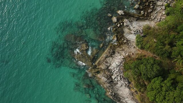 Aerial top view 4k footage by drone of ocean blue waves break on high cliff of a rocky mountain.Dream trip to green island. Outdoor adventure travel to beautiful phuket thiland beach.