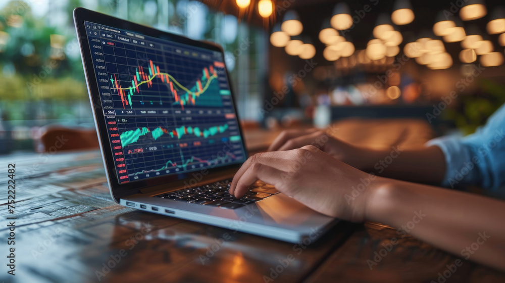 Poster close-up of a person analyzing financial charts on a laptop screen, seated at a wooden table in a ca
