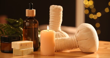 Spa composition. Cosmetic products, herbal bags and burning candle on wooden table, closeup