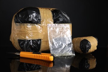 Smuggling, drug trafficking. Packages with narcotics and utility knife on black mirror surface