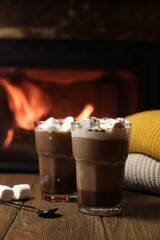 Fototapeta na wymiar Glasses with hot cocoa, marshmallows and sweaters on wooden table near fireplace