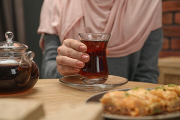 Woman with cup of delicious Turkish tea at wooden table, closeup