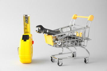 Shopping cart with different construction tools on light grey background