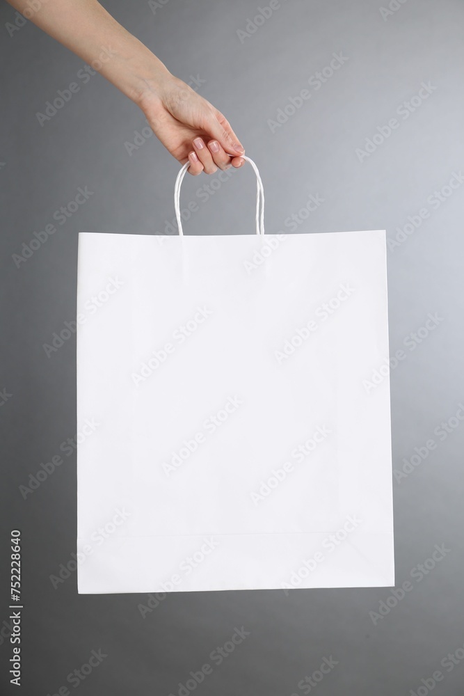 Sticker Woman holding white paper bag on grey background, closeup. Mockup for design