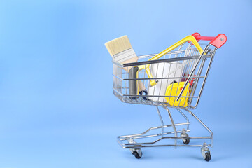 Small shopping cart with paint and renovation equipment on light blue background. Space for text