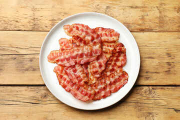 Plate with fried bacon slices on wooden table, top view