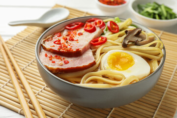 Delicious ramen in bowl and chopsticks on white table, closeup. Noodle soup