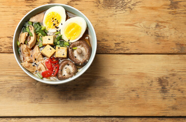 Bowl of delicious ramen on wooden table, top view with space for text. Noodle soup