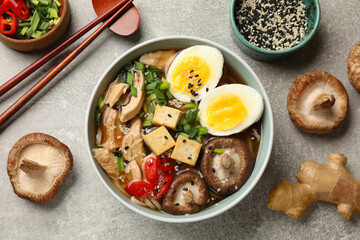 Bowl of delicious ramen and ingredients on grey table, flat lay. Noodle soup