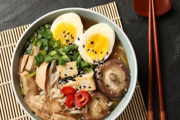 Noodle soup. Bowl of delicious ramen, ingredients and chopsticks on black table, top view