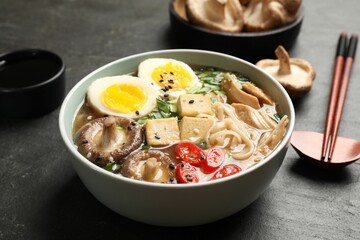Noodle soup. Bowl of delicious ramen, ingredients and chopsticks on black table, closeup