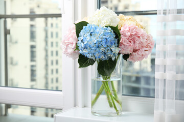 Beautiful hydrangea flowers in vase on windowsill indoors