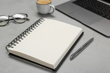Open notebook, pen, laptop and glasses on light grey table