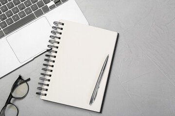 Open notebook, laptop, pen and glasses on light grey table, flat lay