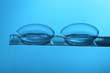 Pair of contact lenses on glass against light blue background, closeup