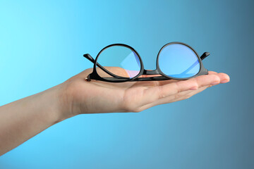 Woman holding glasses with black frame on light blue background, closeup