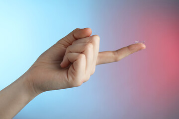 Woman holding contact lens on color background, closeup