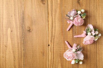 Stylish pink boutonnieres on wooden table, flat lay. Space for text