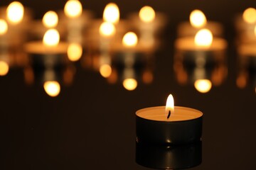 Burning candle on surface in darkness, closeup. Space for text