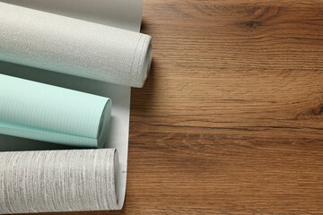 Different wallpaper rolls on wooden table, flat lay. Space for text