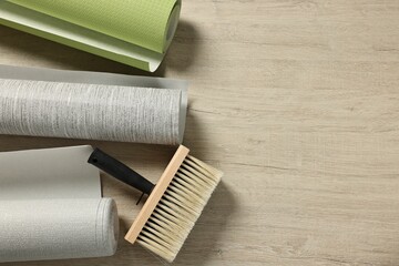 Different wallpaper rolls and brush on wooden table, flat lay. Space for text