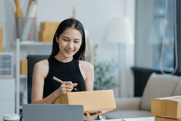 woman start up small business owner writing address on cardboard box at workplace.small business...