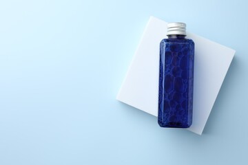 Bottle of cosmetic product on light blue background, top view. Space for text