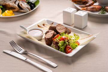 Sliced grilled sausages or kupaty are served with vegetables, salad and ketchup on a white plate. Grill menu concept