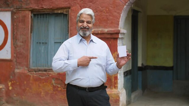 Mature old age man dressed in formal wear ready with his voter identification card to cast his vote in elections. Old businessman proudly showing his voter ID card before elections - responsible ci...