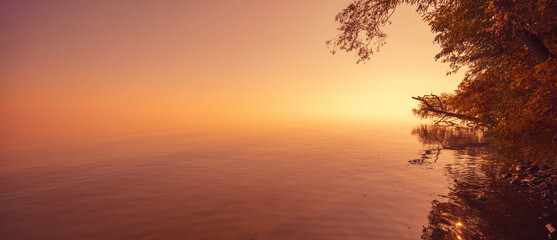 Minimalist landscape. Serene lake during sunrise. Magic sunrise over the lake. Misty early morning. Horizontal banner
