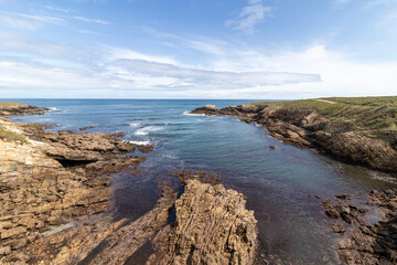 a scenic coastal landscape with rocky shores, calm blue waters, and a clear sky with scattered clouds