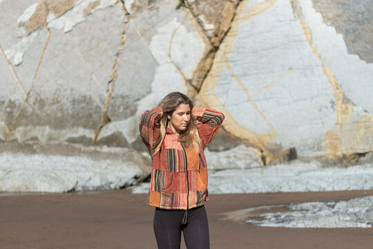 woman wearing a jacket with a patchwork design is standing on a beach. The jacket is red and black, and the woman is looking up at the sky. Concept of calm and relaxation