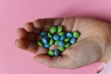 colorful candies in the hand of a child on a pink background