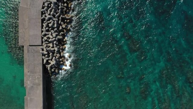 Top aerial drone view of waves crashing on rocky coastline. Blue ocean, wave and impact power. Slowly moving. 4K.


