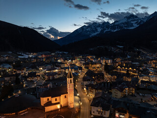 Fototapeta na wymiar Aerial drone view of Andalo town at night with mountains background in winter. Snow covered Italian Dolomites at winter.Ski resort Paganella Andalo, Trentino-Alto Adige, ItalyItalian Dolomites