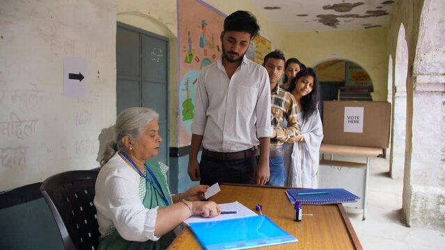 An Indian election officer marks blue ink on the index finger of the voter - state elections  right to vote  voting slip. Candidates standing in the queue at the voting centre to vote - fundamental...