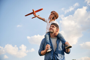 With aviator glasses, playing with toy plane. Father and little son are having fun outdoors