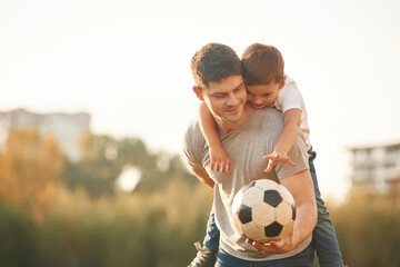 Holding professional soccer ball. Father and little son are playing and having fun outdoors