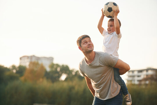 Holding professional soccer ball. Father and little son are playing and having fun outdoors - Powered by Adobe